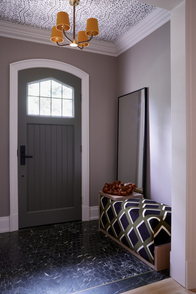 Entrance foyer with stone tile flooring, upholstered bench seating and statement wallpaper and  lighting by Gillian Gillies Interiors
